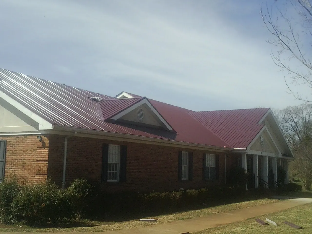 Red metal roof with gabled entries on a long brick building, from a Hail Damage Roof Repair job in Lewisville