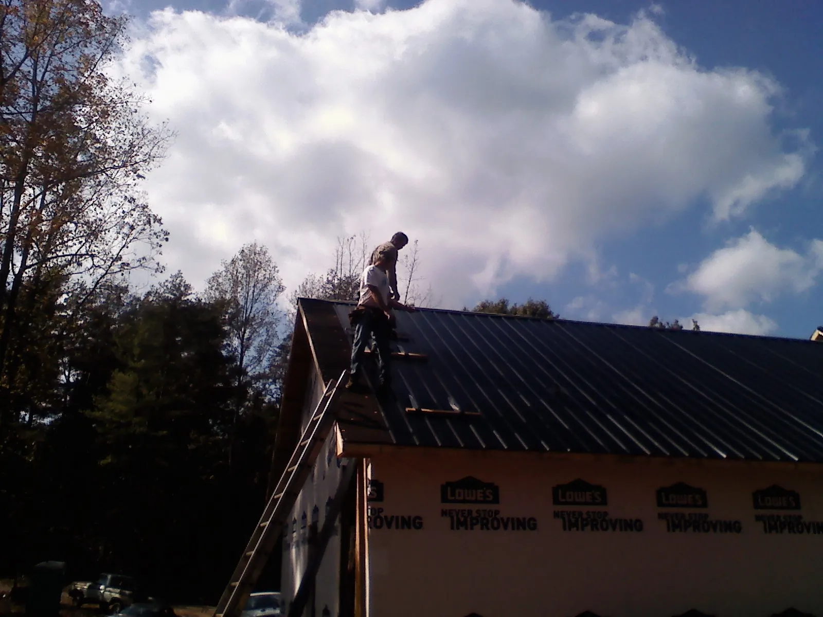 Roofer fastening dark metal panels high against a cloudy sky in Lewisville
